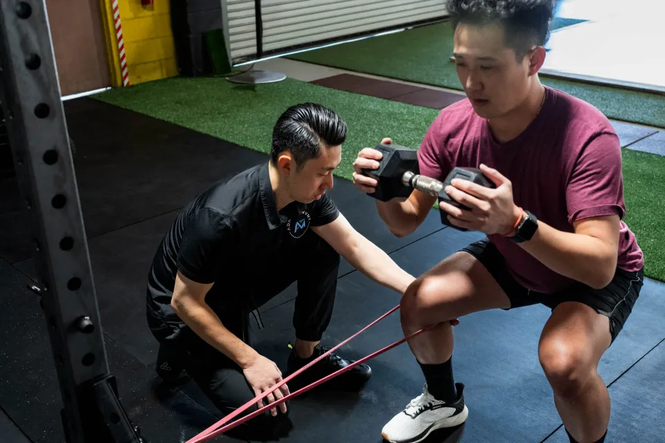 Michael cueing a client's knee with a red resistance band during a goblet squat